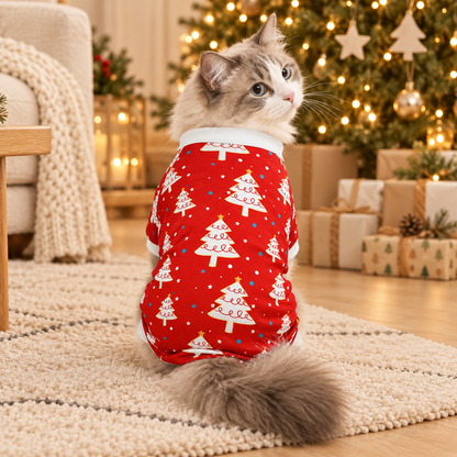 Chat vu de dos portant un pyjama rouge à sapins blancs et col blanc devant un sapin illuminé.
